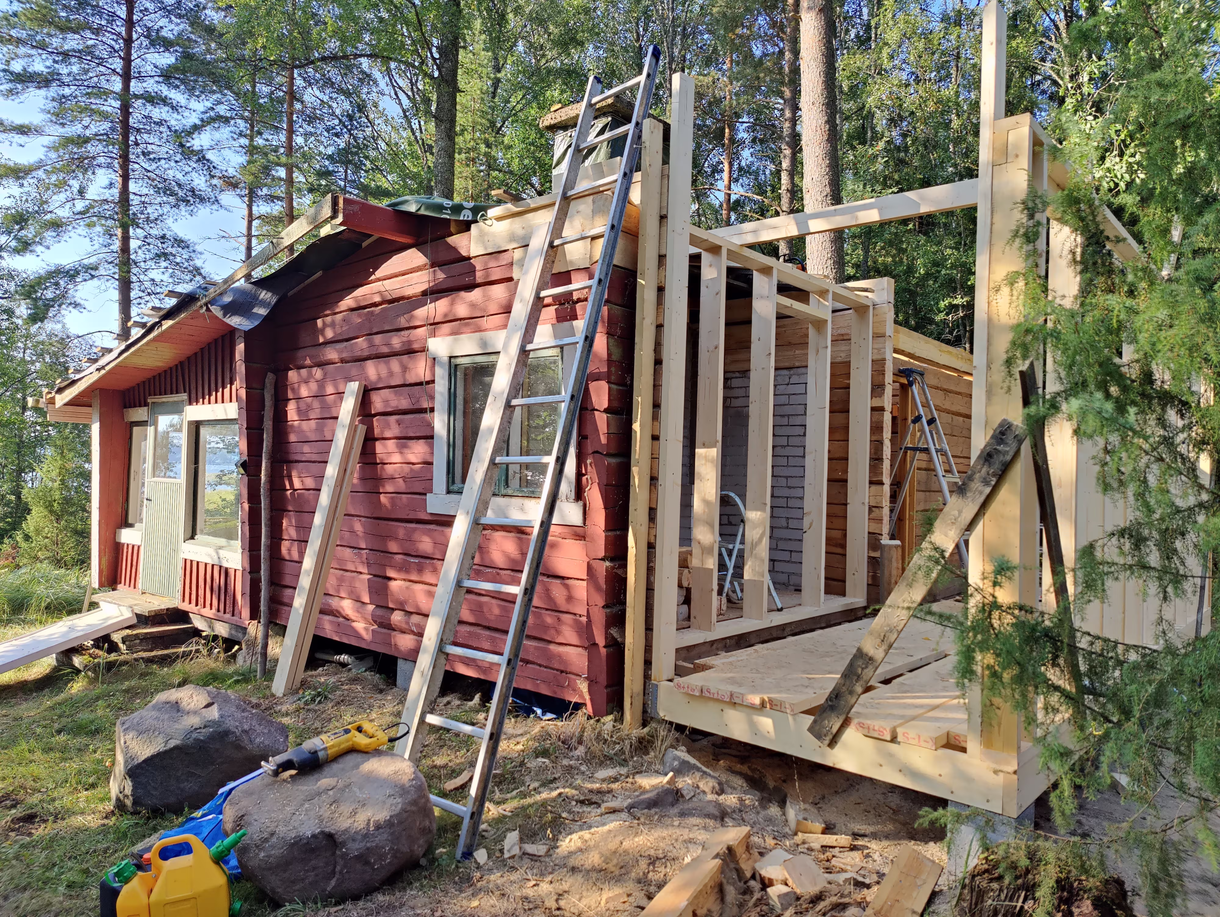 Kuvassa vanha punainen hirsirakennus, josta on purettu kattorakenne täysin, sekä puolet mökistä. Kuvan mukaan mökkiä saneerataan täysin uusiksi. Saunamökin kunnostus. Korjausrakentaminen Helsingissä, Espoossa, Vantaalla ja Kirkkonummella | Jerodel Oy.